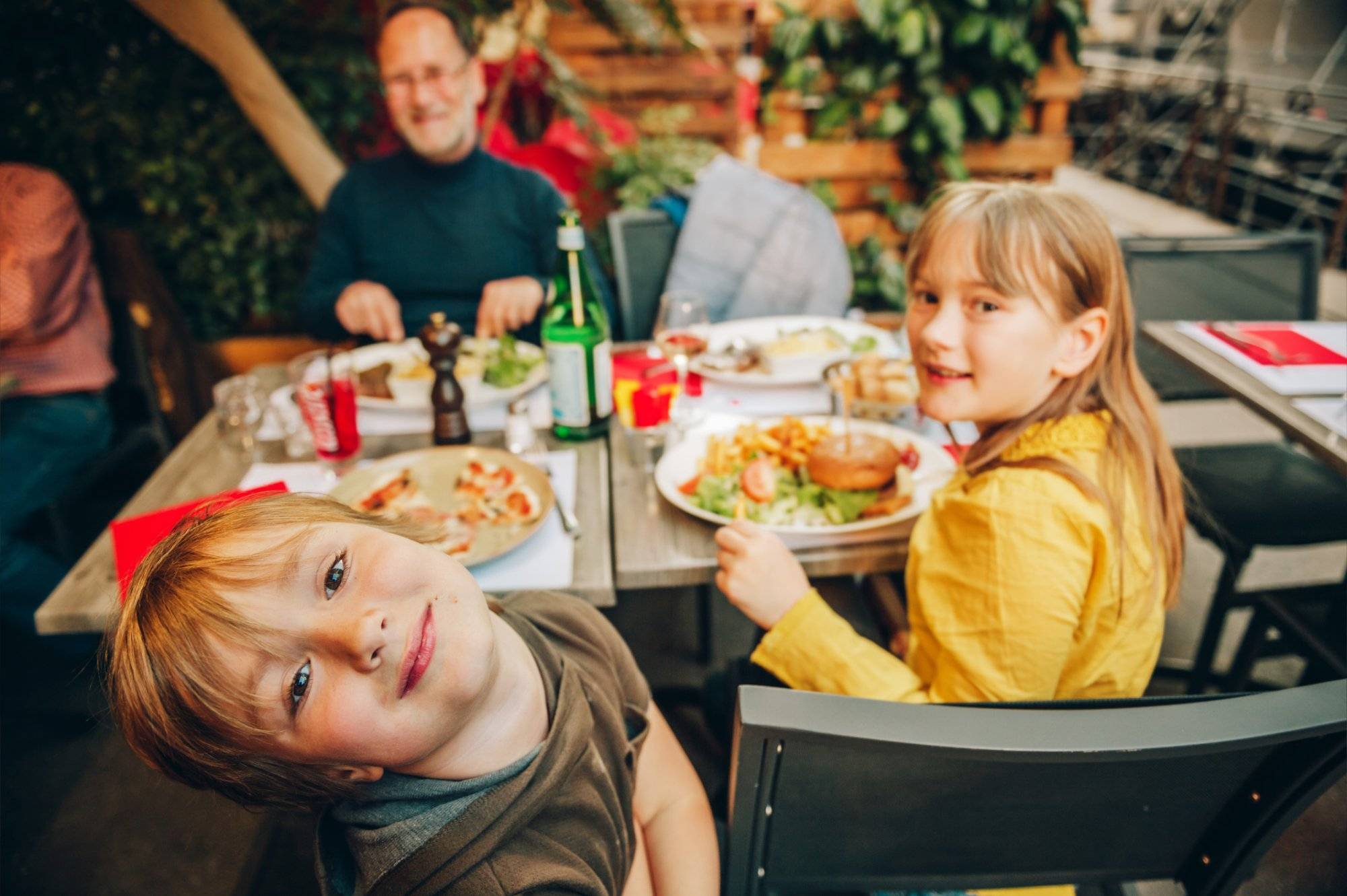 Happy family eating hamburger with french fries and pizza in outdoor restaurant Happy family eating hamburger with french fries and pizza in outdoor restaurant