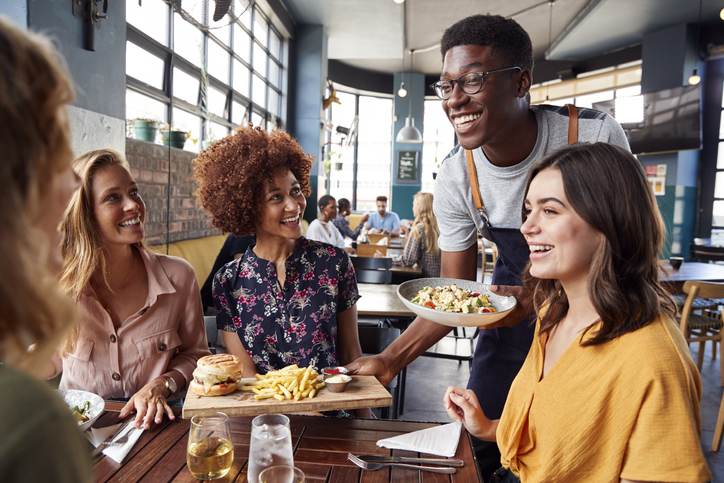 Waiter Serving Group Of Female Friends Meeting For Drinks And Food In Restaurant Waiter Serving Group Of Female Friends Meeting For Drinks And Food In Restaurant