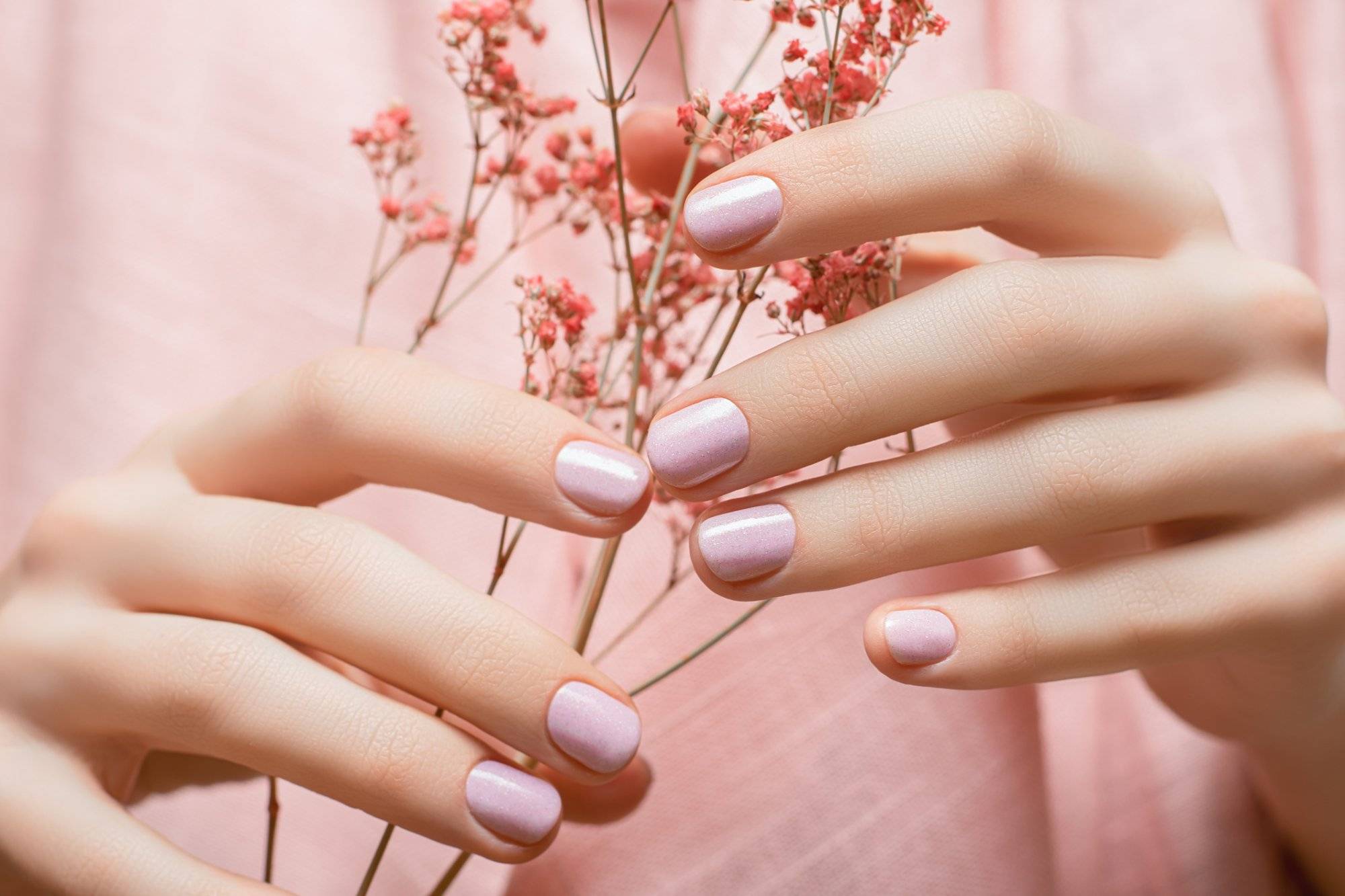 Female hands with pink nail design. Pink nail polish manicure. Woman hands hold orange flowers. Female hands with pink nail design. Pink nail polish manicure. Woman hands hold orange flowers.