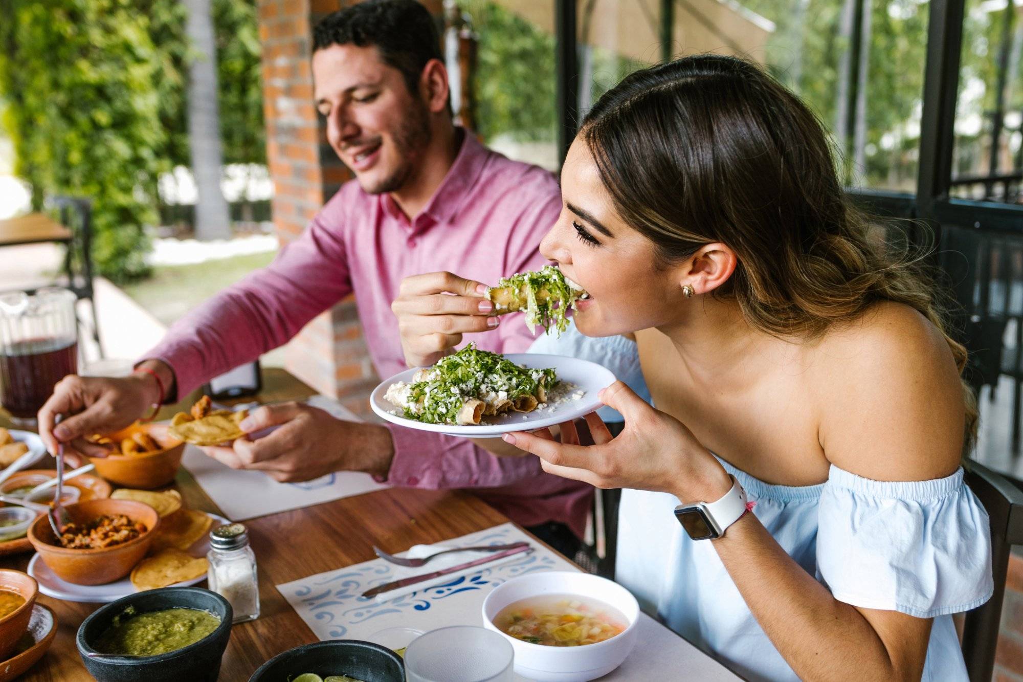 young latin woman eating mexican tacos on a restaurant terrace in Mexico Latin America, feeling happy on a summer day