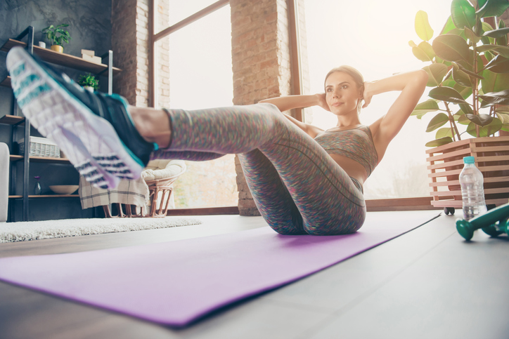 Low-angle photo of attractive sportive pretty strong muscular flexible woman doing sit-ups and holding legs in air trying to keep balance in reflection, sun glare, beam, ray, sunny day